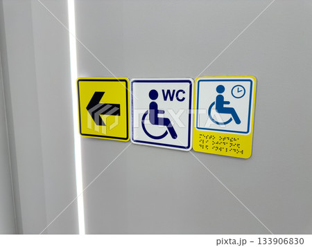Set of signs for people with disabilities on wall. Arrow points to accessible restroom and to waiting area with braille text. Directional navigation for people with mobility issues Set of signs for people with disabilities on wall. Arrow points to accessible restroom and to waiting area with braille text. Directional navigation for people with mobility issues 133906830