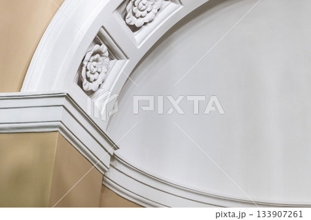A refined white arch and decorative molding detail with floral rosettes 133907261