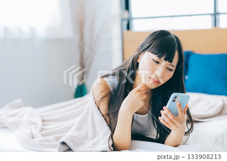 ベッドでスマホを見ながらネガティブな気持ちになる女性 133908213