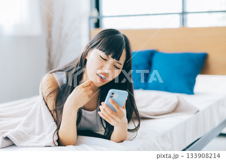 ベッドでスマホを見ながらネガティブな気持ちになる女性 133908214