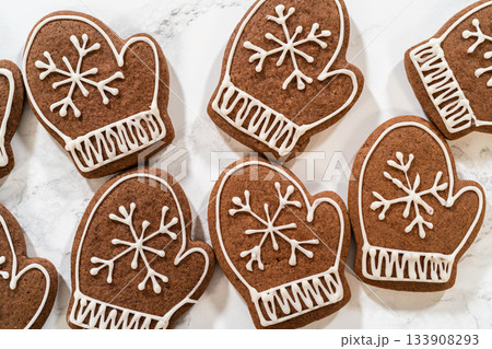 Close-up of beautifully decorated mitten-shaped gingerbread cookies featuring intricate white royal icing designs, arranged on a marble surface. Close-up of beautifully decorated mitten-shaped gingerbread cookies featuring intricate white royal icing designs, arranged on a marble surface. 133908293