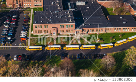 Aerial shot of an American school campus with yellow school buses lined up outside, surrounded by autumn trees and suburban greenery. Aerial shot of an American school campus with yellow school buses lined up outside, surrounded by autumn trees and suburban greenery. 133908300