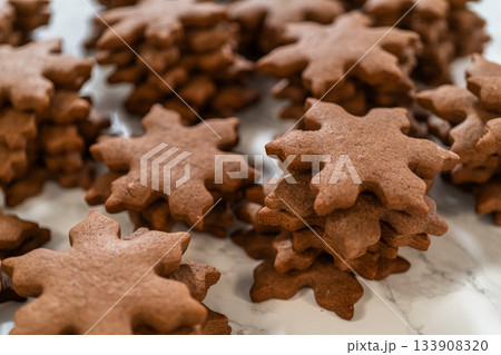 Side view of chocolate ginger snowflake cookies piled together on a parchment-lined surface, showcasing their festive design and holiday charm. Side view of chocolate ginger snowflake cookies piled together on a parchment-lined surface, showcasing their festive design and holiday charm. 133908320