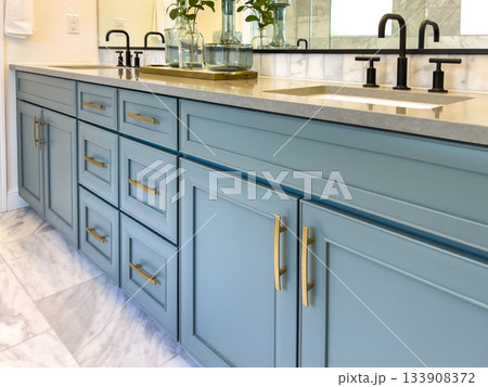 Detail view of a blue bathroom vanity with brass drawer handles. The vanity is topped with a light surface and features clean, modern lines. Detail view of a blue bathroom vanity with brass drawer handles. The vanity is topped with a light surface and features clean, modern lines. 133908372