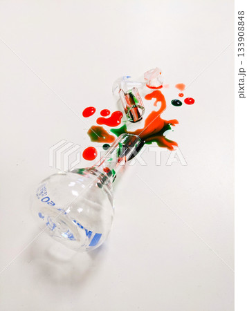 A broken flask and test tube with red and green liquid spills across a clean white background A broken flask and test tube with red and green liquid spills across a clean white background 133908848