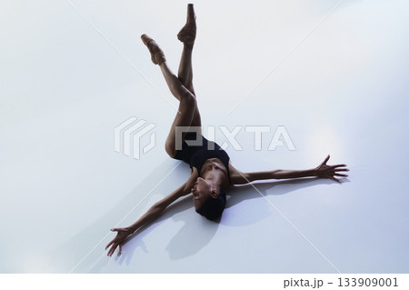 Ballerina lying on floor with legs raised and arms extended outward Ballerina lying on floor with legs raised and arms extended outward 133909001