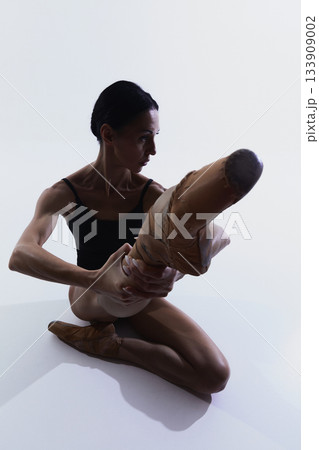 Ballerina seated on floor stretching raised leg while holding foot 133909002