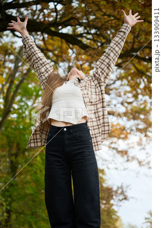 A person relishes the beauty of fall, arms raised high in excitement. Surrounded by vibrant autumn foliage, the scene radiates joy and freedom. A person relishes the beauty of fall, arms raised high in excitement. Surrounded by vibrant autumn foliage, the scene radiates joy and freedom. 133909411