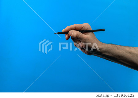 Human hand holding pencil on blue background. Minimalist concept for creativity Human hand holding pencil on blue background. Minimalist concept for creativity 133910122
