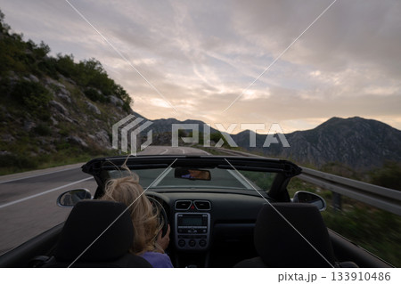 Young woman driving convertible along scenic ocean coast and mountain road at sunset, carefree summer vacation, travel freedom and adventure on coastal highway Young woman driving convertible along scenic ocean coast and mountain road at sunset, carefree summer vacation, travel freedom and adventure on coastal highway 133910486