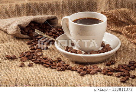 Warm and inviting coffee scene: cup with coffee beans on burlap background Warm and inviting coffee scene: cup with coffee beans on burlap background 133911372