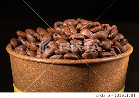 A plastic cup filled with fresh roasted coffee beans on a table A plastic cup filled with fresh roasted coffee beans on a table 133911381
