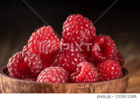 Close-up of a rustic wooden cup filled with fresh raspberries on a wooden table 133911386