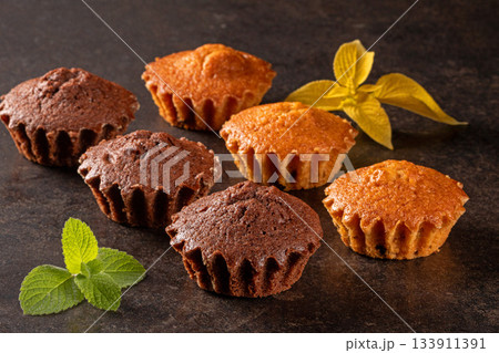 Delicious assortment of muffins garnished with fresh mint leaves on dark background Delicious assortment of muffins garnished with fresh mint leaves on dark background 133911391
