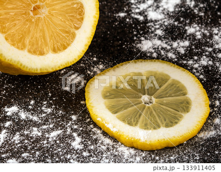Fresh sliced lemon and a sprinkle of powdered sugar on black surface 133911405