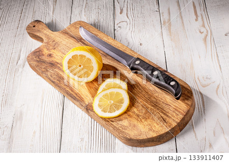 A freshly sliced lemon with a sharp kitchen knife on rustic wooden table 133911407