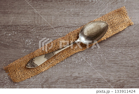 Elegant vintage silver spoon resting on a rustic burlap napkin background 133911424