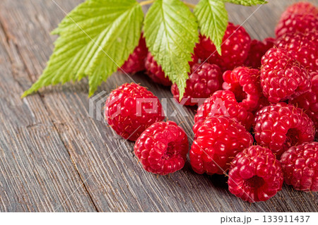 Close-up image of brightly colored ripe raspberries surrounded by green leaves 133911437