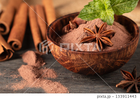 view of a wooden cup filled with cocoa powder, star anise, and cinnamon sticks view of a wooden cup filled with cocoa powder, star anise, and cinnamon sticks 133911443