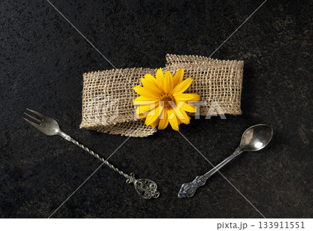 Artistic arrangement of vintage cutlery with floral accent and textured ribbon 133911551