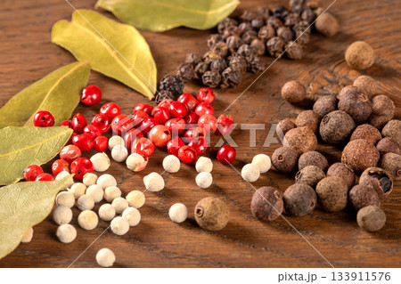 A display of white, red, black pepper, and bay leaves on a rustic table 133911576