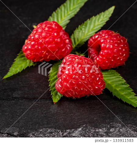 Close-up of three vibrant raspberry berries on a dark stone background Close-up of three vibrant raspberry berries on a dark stone background 133911583