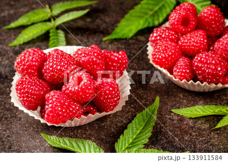 Vibrant bright red raspberry berries with green leaves against a black background Vibrant bright red raspberry berries with green leaves against a black background 133911584