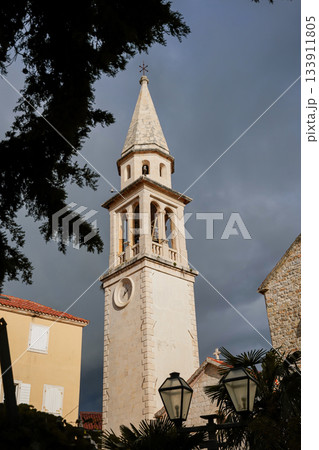 Photo taken from a low angle showing a church tower in the historic old town of Budva, Montenegro. Focus on medieval architecture, European heritage, and iconic city landmarks. 133911805