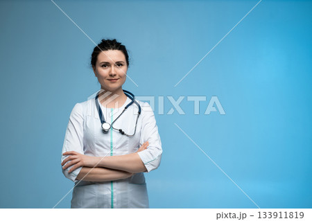 Female doctor with stethoscope standing confidently in white uniform on clean blue studio background Female doctor with stethoscope standing confidently in white uniform on clean blue studio background 133911819