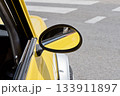 Closeup of yellow vintage car side mirror and door frame by city crosswalk in bright daylight 133911897