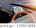 Close view of vintage car dashboard with wooden steering wheel, large analog tachometer and chrome details, warm sunlight flare 133911898