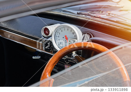 Close view of vintage car dashboard with wooden steering wheel, large analog tachometer and chrome details, warm sunlight flare Close view of vintage car dashboard with wooden steering wheel, large analog tachometer and chrome details, warm sunlight flare 133911898