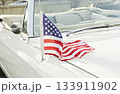 Small American flag mounted on antenna of white vintage convertible, stars and stripes draped over hood in bright daylight 133911902