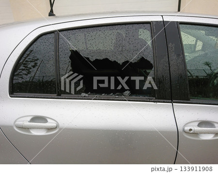 Car break in shattered smashed side window on wet silver sedan. burglary surge tied to economic strain, theft risk rising across neighborhoods 133911908