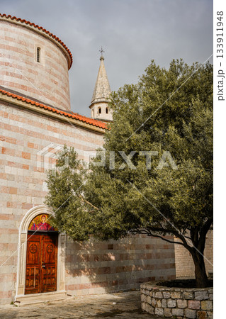 Photo of a large olive tree standing next to a historic church in the Old Town of Budva, Montenegro. Highlights medieval architecture, stone walls, and Mediterranean charm. Ideal for travel, European Photo of a large olive tree standing next to a historic church in the Old Town of Budva, Montenegro. Highlights medieval architecture, stone walls, and Mediterranean charm. Ideal for travel, European 133911948