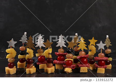 Assorted canapes with tomatoes, mozzarella cheese, salami, pineapple, olives and grapes on a marble table. Christmas and New Year's dishes, a set of snacks for the festive table. Assorted canapes with tomatoes, mozzarella cheese, salami, pineapple, olives and grapes on a marble table. Christmas and New Year's dishes, a set of snacks for the festive table. 133912272