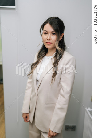 Young Asian woman standing in light business suit with professional demeanor, portraying concept of business professional, medical staff, or successful entrepreneur, looking at camera. 133912776