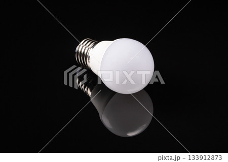 Elegant white matte led bulb reflecting on a black mirrored surface 133912873