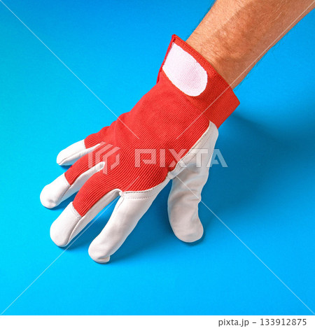 A man's hand wearing a red work glove set against a vibrant blue background A man's hand wearing a red work glove set against a vibrant blue background 133912875