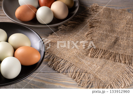 Rustic wooden table displaying vibrant, eco-friendly multicolored chicken eggs 133912960