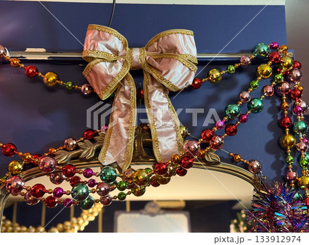 Velvet bow with golden trim among colorful Christmas bead garlands on festive decor. Holiday glamour, joyful winter brightness, celebration sparkle and decorative seasonal charm. 133912974