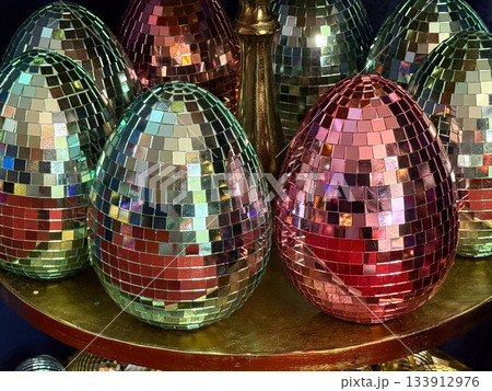 Christmas Disco mosaic egg ornaments arranged together on golden plate under soft lights. Holiday glamour, modern Christmas styling, party sparkle and festive decorative energy. Christmas Disco mosaic egg ornaments arranged together on golden plate under soft lights. Holiday glamour, modern Christmas styling, party sparkle and festive decorative energy. 133912976