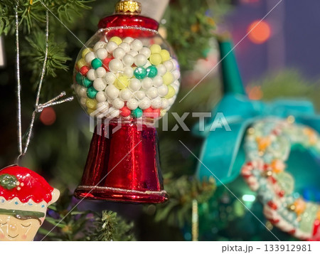 Retro gumball machine ornament with colorful candy balls hanging on Christmas tree. Fun playful holiday mood, cheerful winter celebration and sweet festive nostalgia energy. 133912981