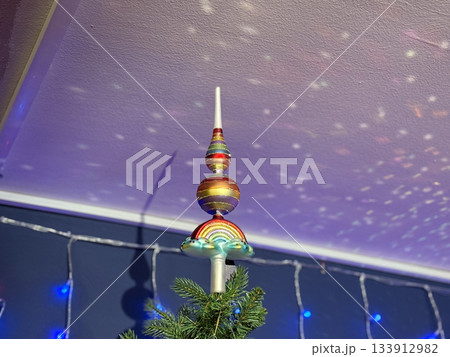 Colorful Christmas tree topper with shimmering projection on ceiling in soft light. Seasonal magic, winter celebration fantasy, joyful home spirit and festive ambience. 133912982