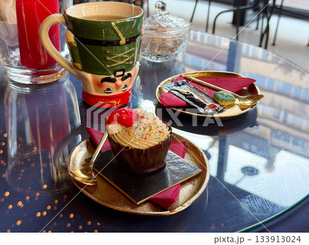 Christmas dessert setting with nutcracker mug and festive cupcake. Warm celebration, seasonal charm and joyful winter storytelling enhancing cozy atmosphere and decorative holiday mood Christmas dessert setting with nutcracker mug and festive cupcake. Warm celebration, seasonal charm and joyful winter storytelling enhancing cozy atmosphere and decorative holiday mood 133913024