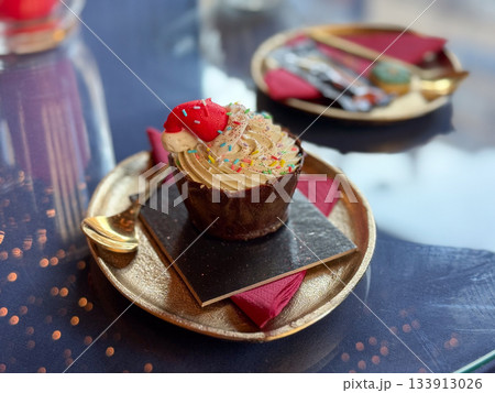 Festive cupcake served on a golden plate in a holiday cafe. Sweet celebration, joyful tradition and warm Christmas storytelling creating cozy seasonal mood and delightful winter atmosphere Festive cupcake served on a golden plate in a holiday cafe. Sweet celebration, joyful tradition and warm Christmas storytelling creating cozy seasonal mood and delightful winter atmosphere 133913026