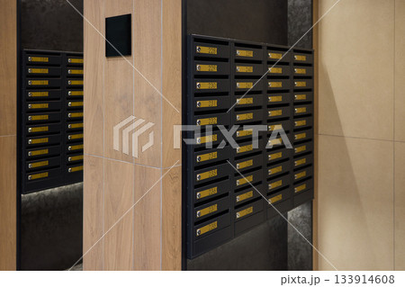 Neatly arranged mailboxes along corridor walls, Orderly line of mailboxes in city housing corridor, Well-organized row of mailboxes with brass plates in urban apartment hallway 133914608