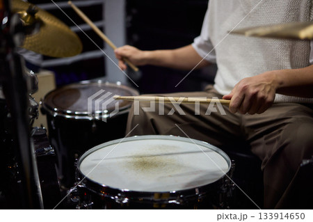 Drummer hands striking snare drum with sticks, captured midperformance showing motion blur, textured drumhead, casual stage clothing and focused groove driving live club energy 133914650