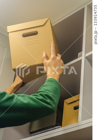 Man Placing Cardboard Storage Box on Closet Shelf Man Placing Cardboard Storage Box on Closet Shelf 133914735