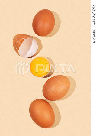 An artistic composition of brown eggs on a pastel yellow background with one cracked egg An artistic composition of brown eggs on a pastel yellow background with one cracked egg 133914847